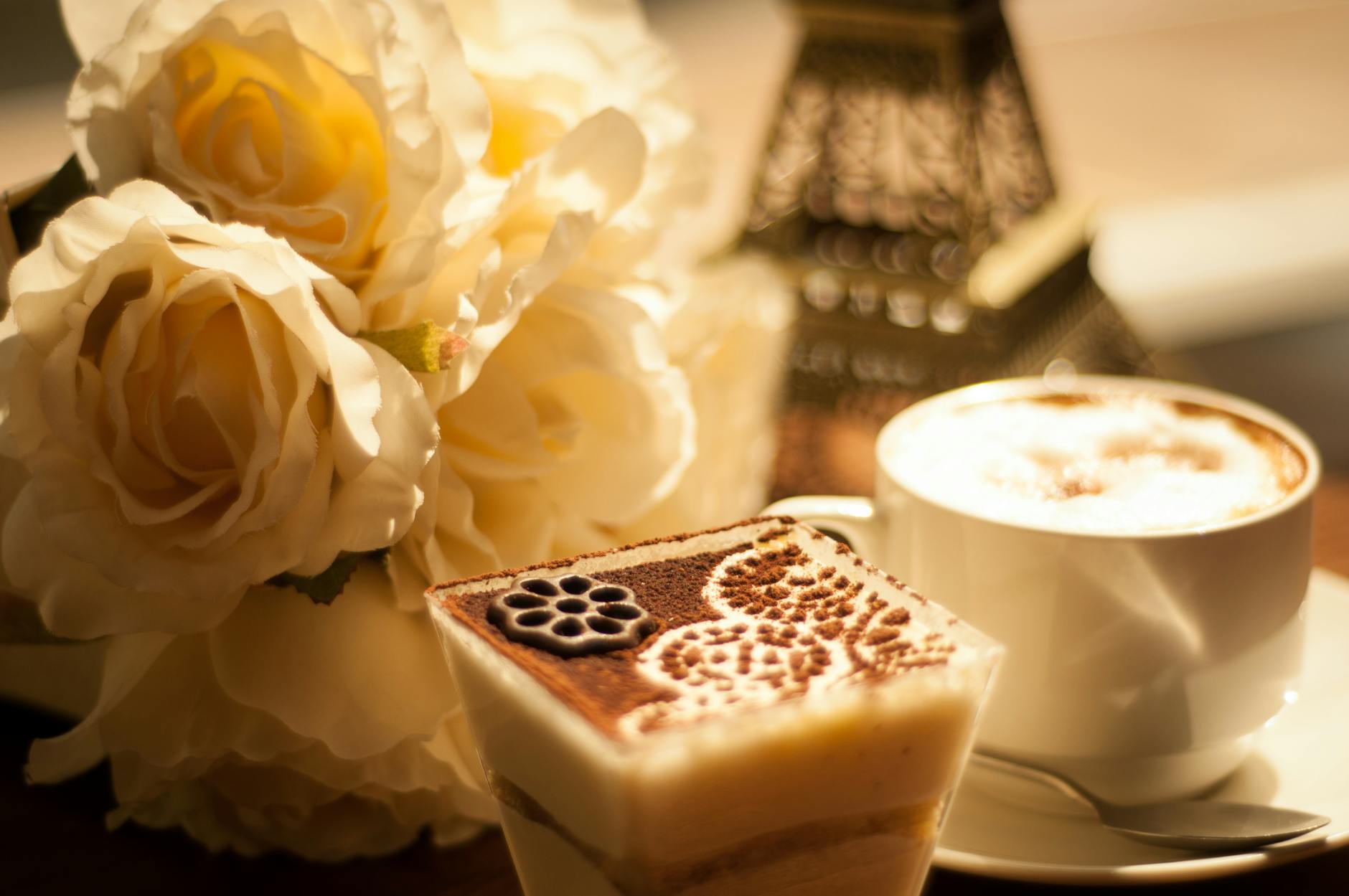 Kawa z kremową pianką i deserem przy białych różach na stole