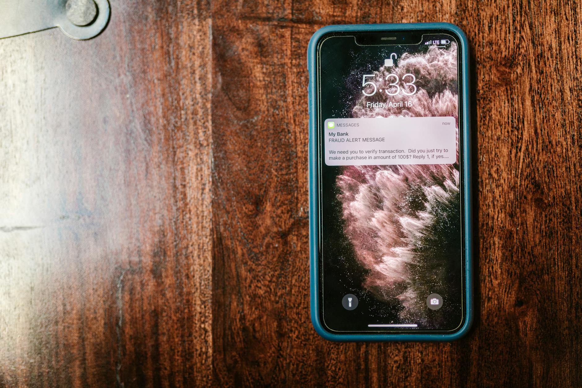 Smartfon na drewnianym stole z wyświetlonym alertem o oszustwie
