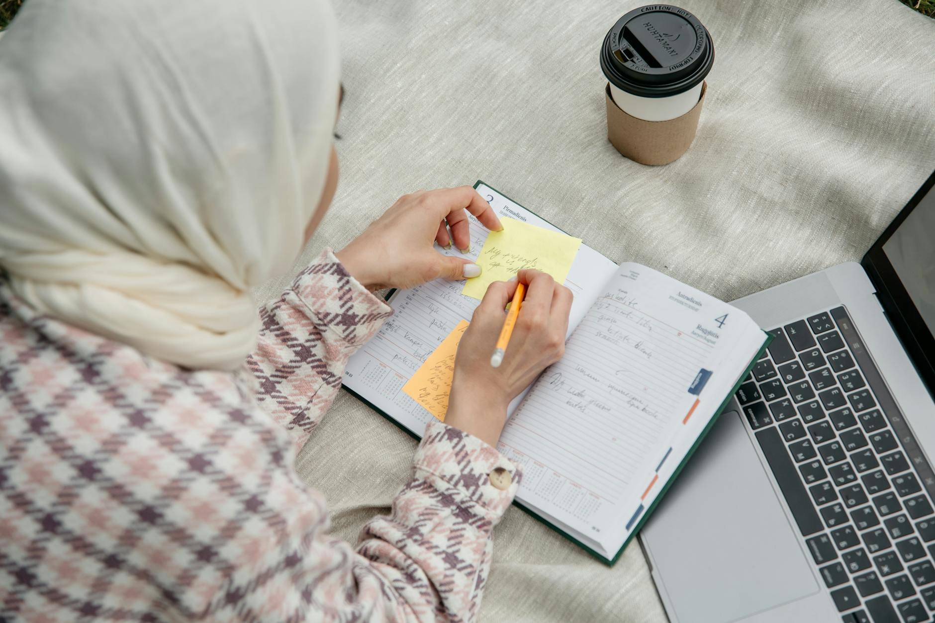Kobieta w hidżabie planuje weekend w notesie przy laptopie na zewnątrz