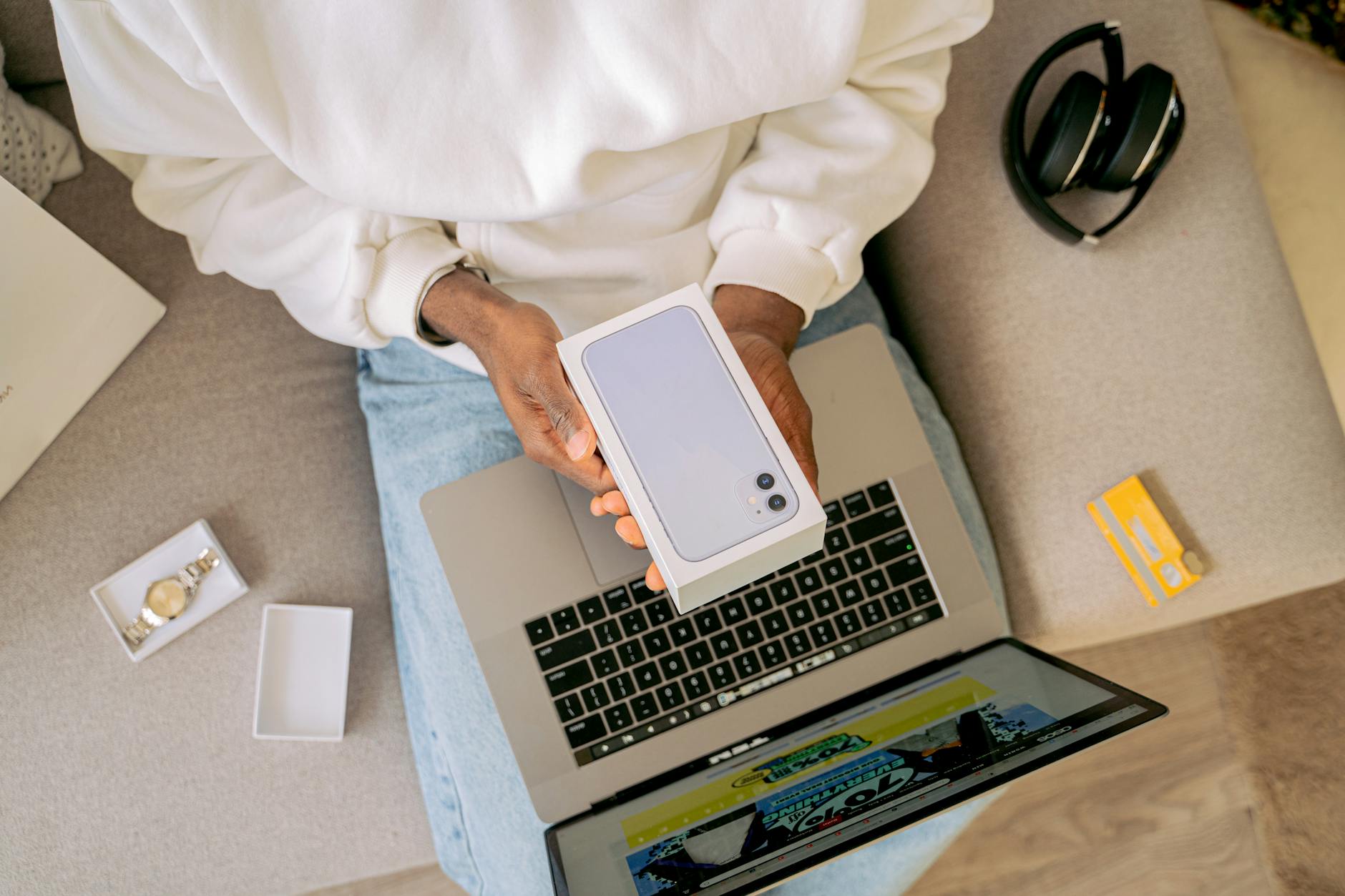 Osoba na kanapie rozpakowuje nowy smartfon obok otwartego laptopa