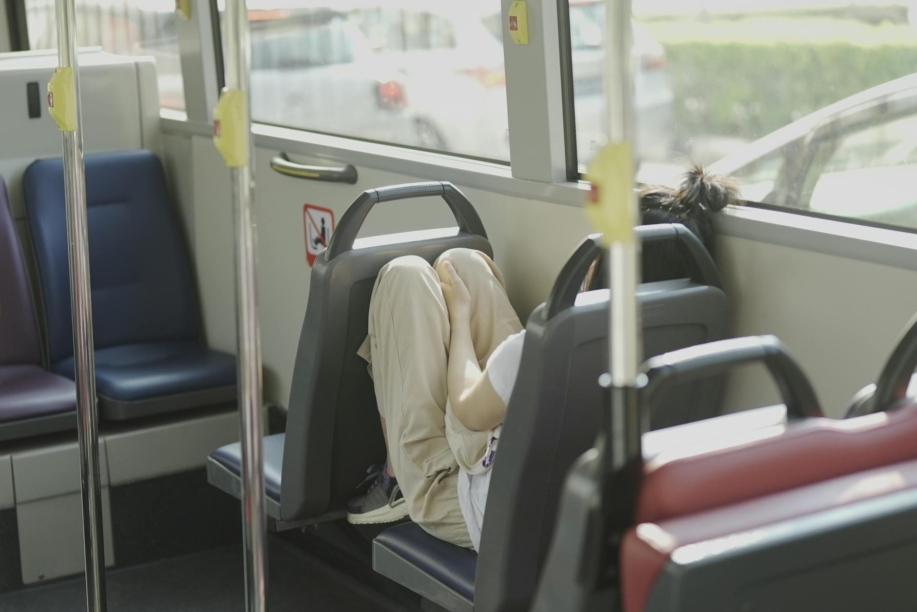 Osoba śpi skulona na siedzeniu autobusu w dzień