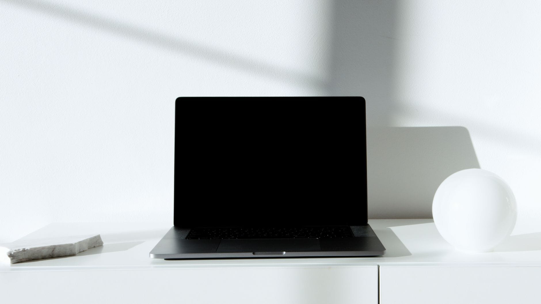 Czarny laptop na białym, minimalistycznym biurku w naturalnym świetle