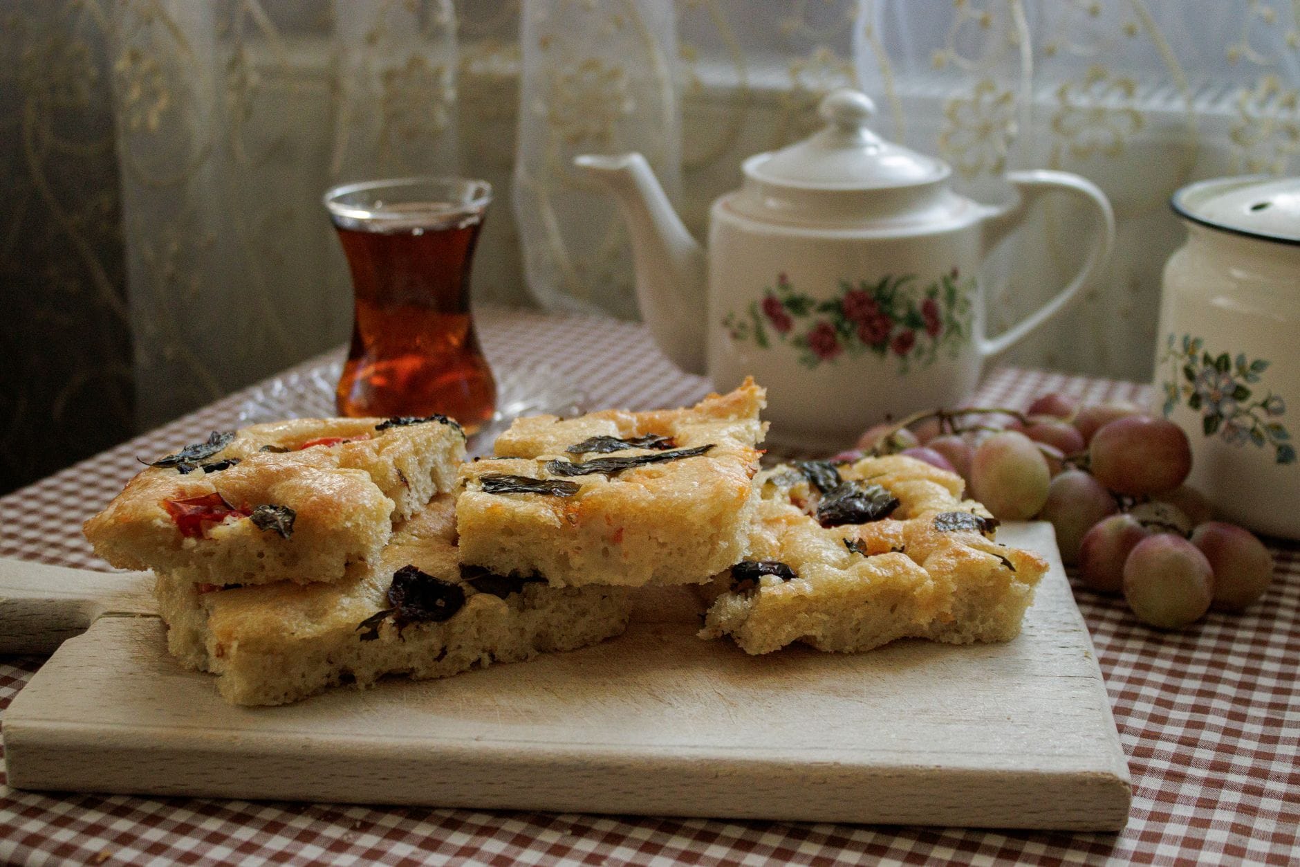Rustykalna domowa focaccia na desce obok herbaty i winogron w kuchni