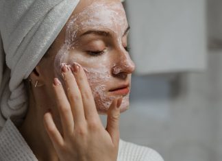 Peeling enzymatyczny czy mechaniczny: co wybrać przy cerze wrażliwej? Kobieta nakładająca glinkową maseczkę na twarz w domu