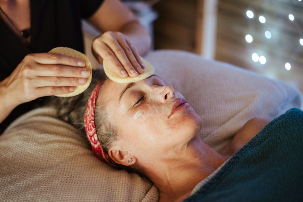 Kosmetyczka zmywa gąbką maskę z twarzy kobiety w spa